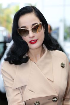 a woman with dark hair wearing sunglasses and a trench coat