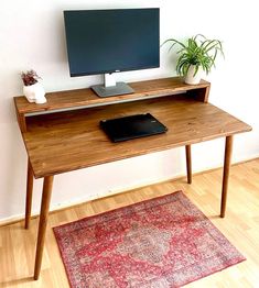 a wooden desk with a computer monitor and laptop on it next to a red rug