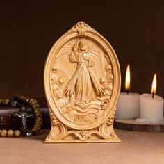 an image of the virgin mary with three candles behind it on a brown table next to some books