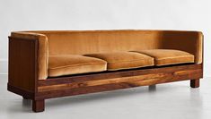 a wooden couch with four cushions on it's back and sides, in an empty room