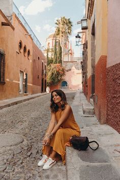 a woman sitting on the side of a street next to a building and holding a handbag