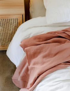 an unmade bed with white sheets and pink blankets on top of it, next to a night stand