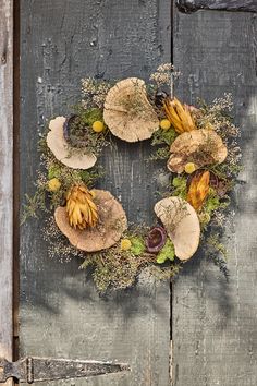 a wreath made out of leaves and flowers on the side of a wooden door with a pair of scissors