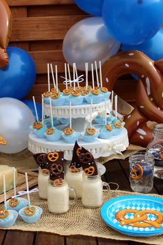 a table topped with cake and desserts covered in blue frosting next to balloons