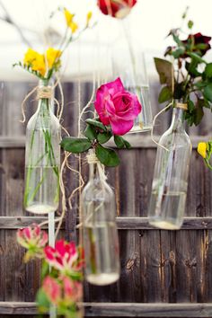 several vases with flowers in them sitting on a wooden fence line, one is filled with water and the other has no leaves