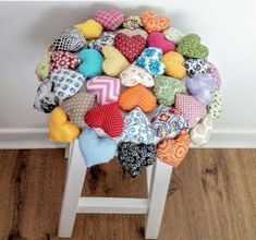 a pile of heart shaped cushions sitting on top of a white stool next to a wall