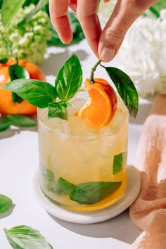 someone is placing an orange slice on the top of a glass with ice and mint