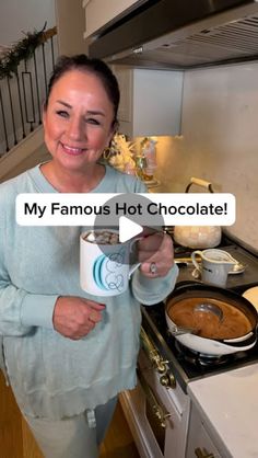 a woman holding a coffee mug in her hand while standing in front of a stove