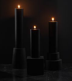 three black candles are lit in the dark