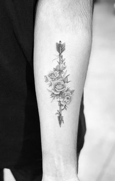 a cross with roses and an arrow tattoo on the left inner forearm is shown in black and white