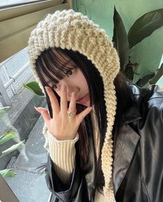 a woman wearing a knitted hat and holding her hand up to her face while standing next to a window