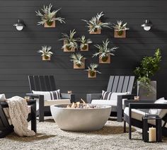 an outdoor fire pit surrounded by chairs and potted plants on the wall behind it