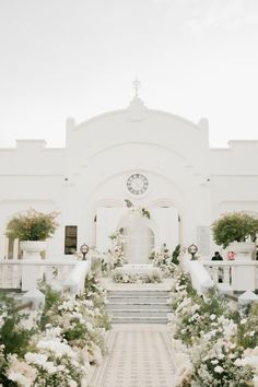 a white church with flowers and stairs leading up to the front door that has a clock on it