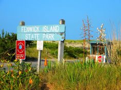 a street sign on the side of a road near grass and flowers in front of a blue sky