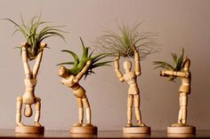 three wooden figurines are holding plants in their hands and standing on one leg