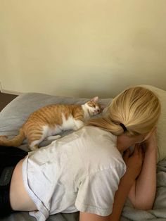 a woman laying on top of a bed next to a orange and white cat in her lap