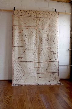 an old rug hanging on a wall in a room with wood floors and white brick walls