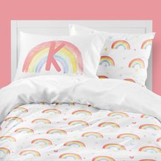 a bed with white sheets and rainbows on the pillowcase in front of a pink wall