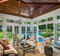 a living room filled with lots of furniture and windows next to a swimming pool in the background