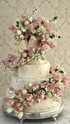 a three tiered wedding cake with pink flowers on the top and white icing