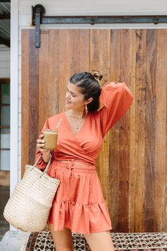 a woman in an orange dress is holding a straw bag and drinking from a cup