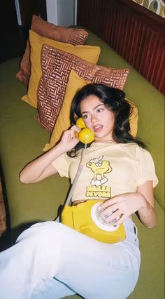 a woman sitting on a couch talking on a phone and holding a yellow object in her hand