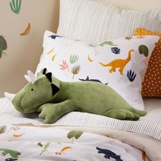 a green dinosaur pillow laying on top of a bed next to a white and orange pillow