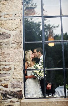 a bride and groom kissing in front of a window