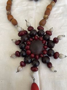 a necklace made out of beads and other items on a white tablecloth with a red bead in the center