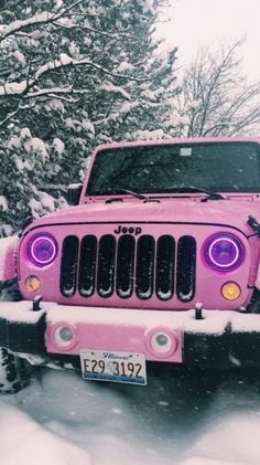 a pink jeep is parked in the snow with its lights on and it's hood up