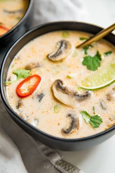 two black bowls filled with soup and topped with mushrooms, cilantro, green peppers, and lime