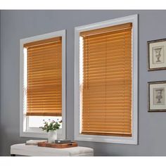 two windows with wooden blinds in the corner and pictures on the wall next to them