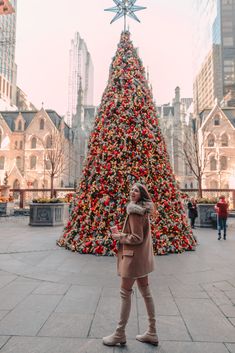 a woman standing in front of a large christmas tree with lights on it's sides