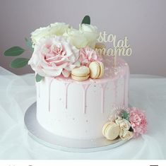 a white cake with pink flowers and macaroons on the top is decorated with gold letters