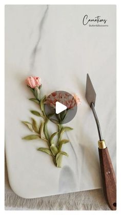 a knife and some flowers on a white plate with a wooden spoon next to it