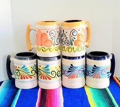 four colorful coffee mugs sitting on top of a blue table cloth next to each other