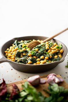 a skillet filled with chickpeas and spinach on top of a cutting board