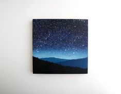 a painting hanging on the wall with mountains in the background and stars above it,