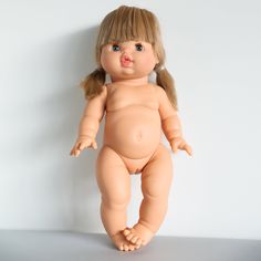 a baby doll with blonde hair is posed on a white surface and looks at the camera