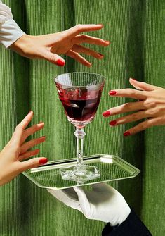 three hands reaching for a glass of wine on a clear serving tray with green cloth