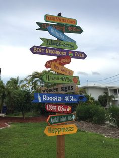 a wooden sign with many different colored signs on it's side in front of a house