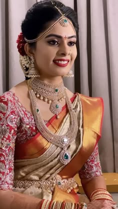 a woman in a red and gold sari with jewelry on her neck, smiling at the camera