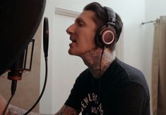 a man with tattoos and headphones on singing into a microphone in a recording studio