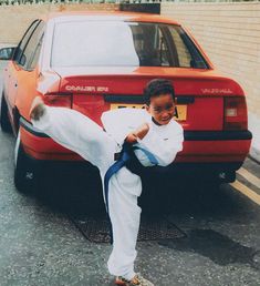 a young boy doing karate in front of a red car