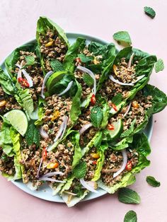 a white plate topped with lettuce and meat salad on top of a pink table