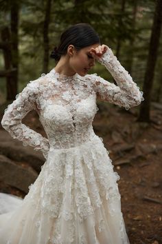 a woman in a wedding dress standing in the woods with her hands on her head