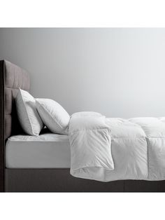 a bed with white sheets and pillows on top of it in a gray room next to a wall