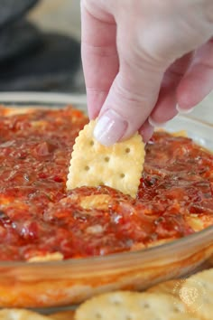 a person dipping a cracker into a bowl of chili cheese dip with crackers