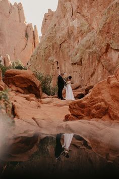 a bride and groom standing in front of some rocks with their reflection in the water