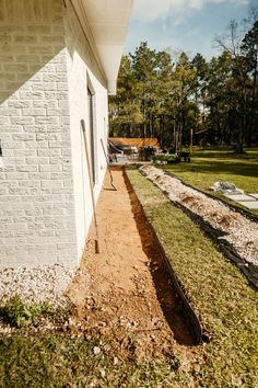 the side of a house with grass and dirt on the ground next to an empty lawn